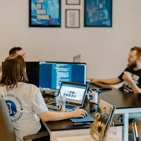 Team members at a shared desk working across laptops and monitors
