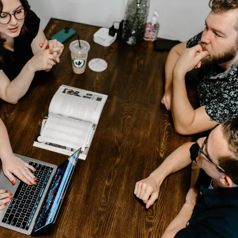 Four team members around a conference table with a laptop and an open magazine