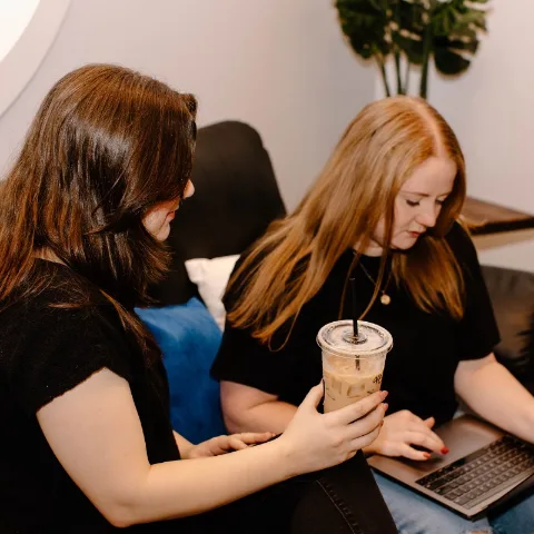 Two team members looking over a laptop together on the studio couch
