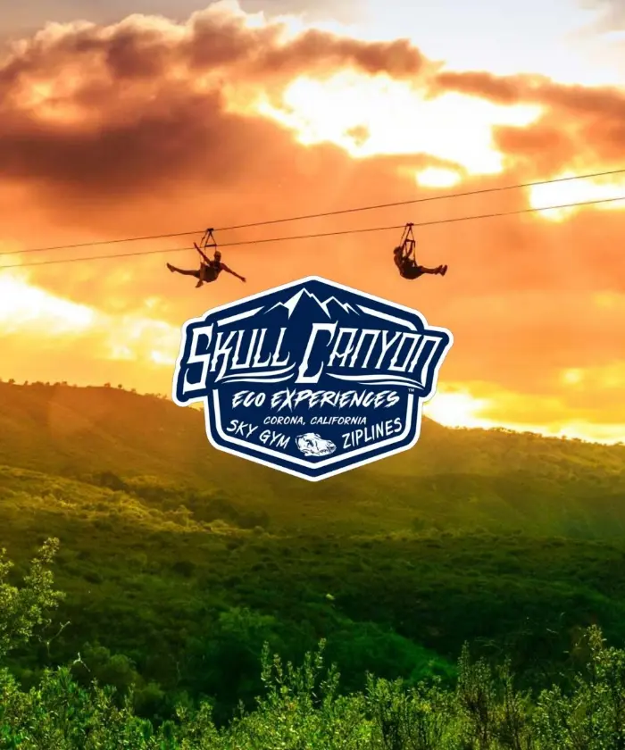 The Skull Canyon Ziplines logo over two riders crossing a canyon at sunset